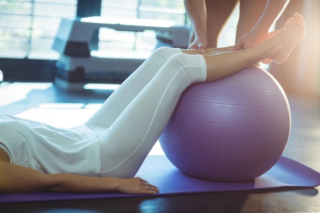 A person is sitting on the floor with their feet on an exercise ball.